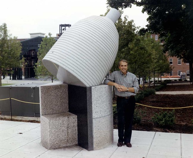 A man standing next to a granite bobbin sculpture.
