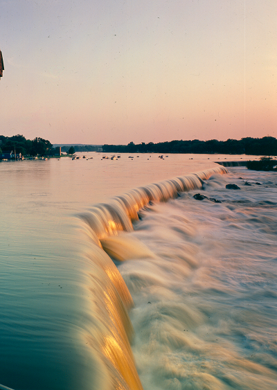 A bright orange sun sets over the rushing water at Pawtucket Falls