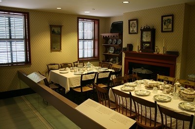 A view of a historic dining room in a boardinghouse. The room is full of tables, chairs, and place settings