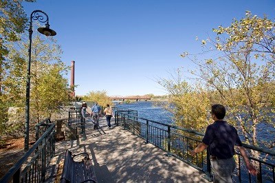 A group of people talk a walk along a paved walkway next to a large river.