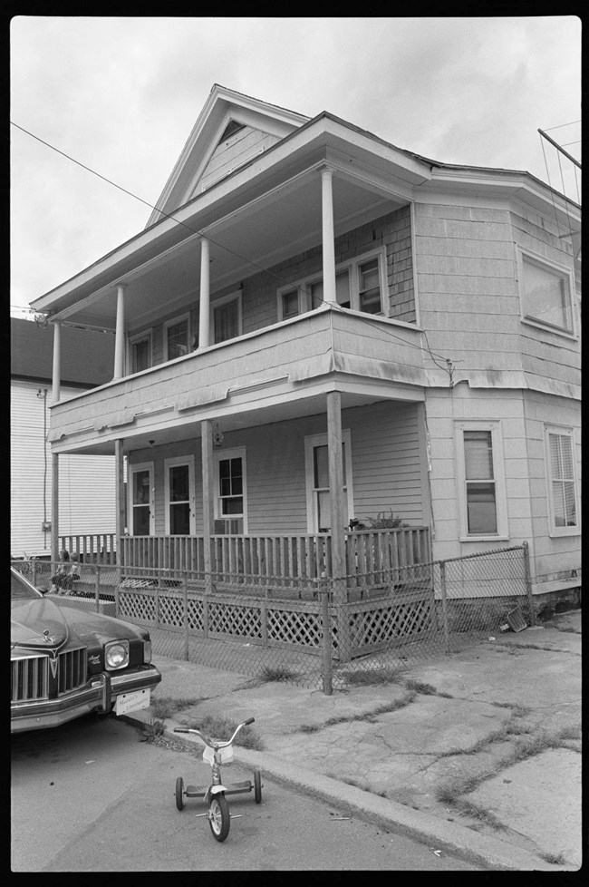 A two story house with balconies off the front. A tricycle and car are in view.