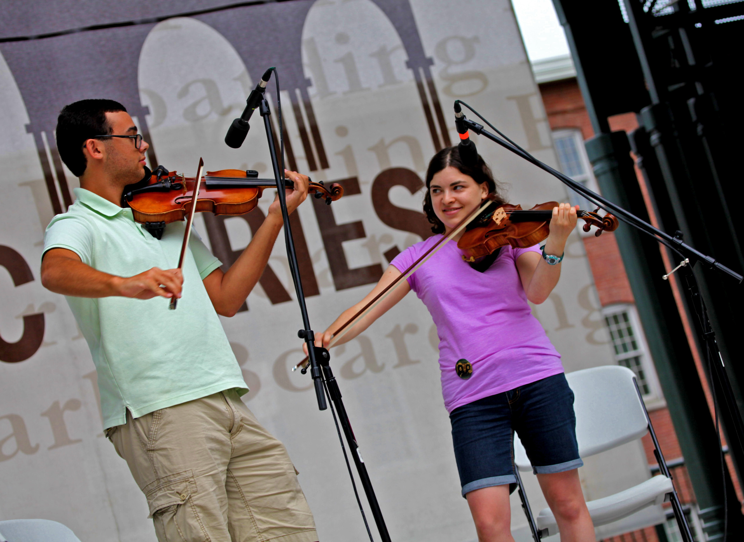Man on the left plays fiddle while looking at a women to the right, also playing a fiddle at the 2017 Banjo and Fiddle Contest 2017 Banjo and Fiddle Contest at Boarding House Park