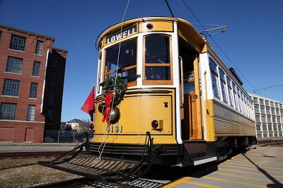 A bright yellow trolley car #4131 is center image. ON the front is a green wreath with a red ribbon in the center of the front of the trolley, below the windshield.