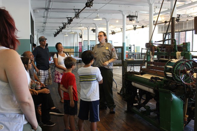 A ranger demonstrates how a loom works to a group of children and parents