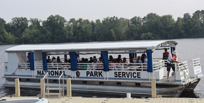 A group of people sit on a pontoon boat as a ranger and first mate prepare to travel along the river.