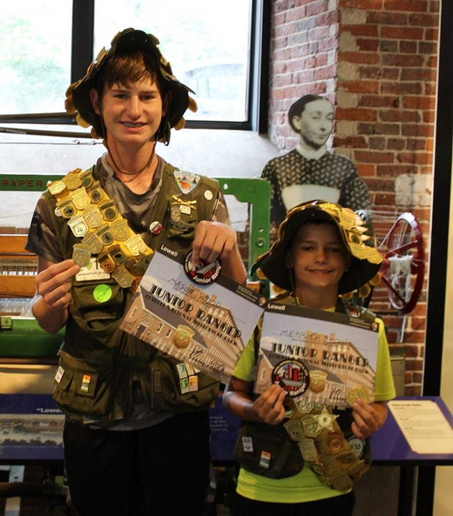 Two junior rangers stand side by side displaying certificates and badges