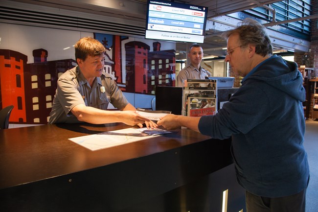 A park ranger gives a paper map to a male visitor at the Visitor Center information desk