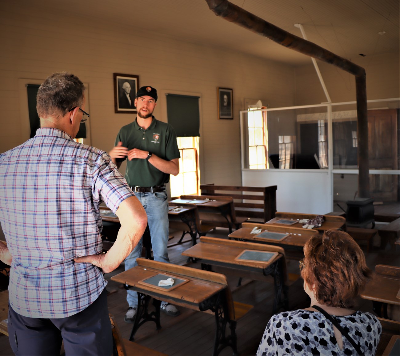 A tall young man talks with visitors about the one-room Junction School they are standing in.