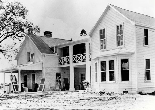 Black and white photo of a two-story frame house surrounded by construction materials.