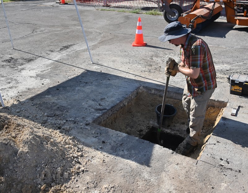 A man stands in a square, two foot hole cut in asphalt.