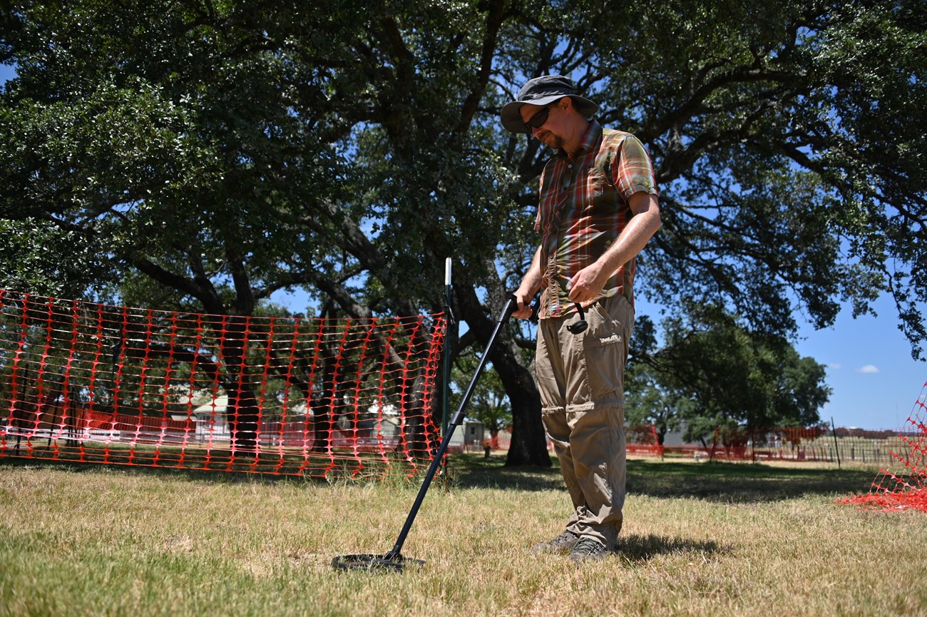 A man stands in a grassy area with a long metal wand.