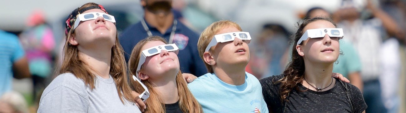 People wearing eclipse glasses looking up at sky.
