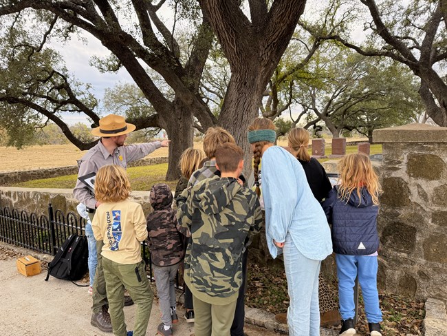 A park ranger stands pointing into a cemetery with children.