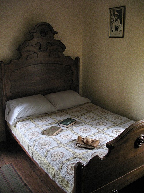 Books and baseball glove sit on a quilt-covered bed with a tall, wooden headboard.