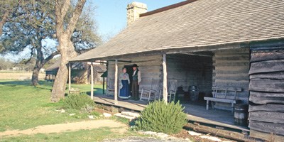 Volunteers in 1860s clothing stand on the porch of the Johnson Settlement cabin