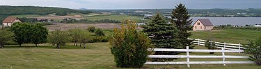 The landcape is filled with trees, homes, and the river with a white fence in the foreground.
