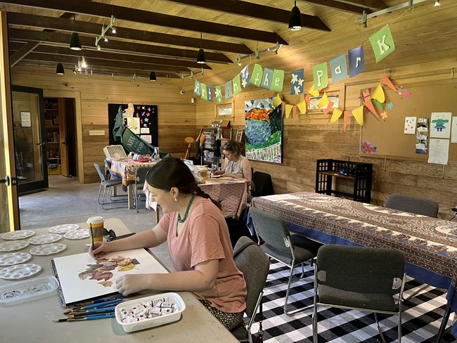 artists work on art in the artist studio, banner behind them reads "art in the park"