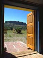 A wooden door, framed by the darkness inside the church, opens out onto a brick porch and the bright sun of the outdoors.