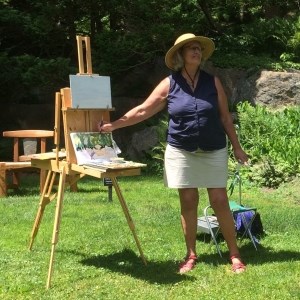 woman points to easel with painting outdoors