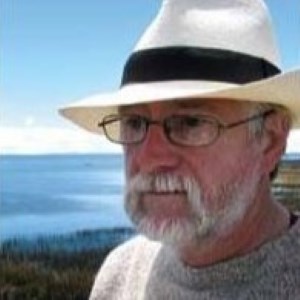headshot of man in hat in front of beach