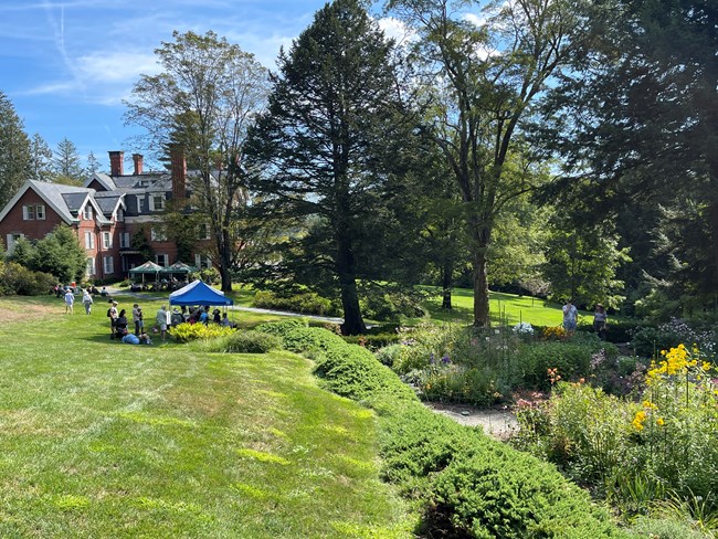 view of landscape with mansion in the background, right has formal garden and left has manucured lawn on hill