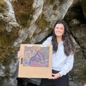 woman poses with illustration of cave in front of a cave entrance