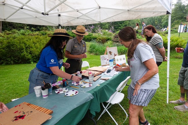 Ranger with visitors paint under a tent with garden in background