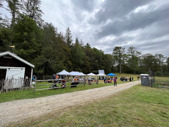 Large field with 4 pop up tents in center, small shed in left foreground, portopotty on right