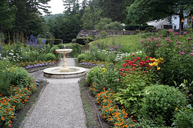 Formal four square garden with blooming flowers and white marble fountain in the center