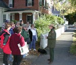 Standing next to an old brick and white clapboard house, a park ranger talks with 11 people. Standing next to an old brick and white clapboard house, a park ranger talks with 11 people.