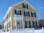 This yellow-brick house with white trim and black shutters stands proudly in the winter sun.