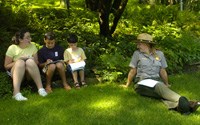 Three children and a park ranger sit in the shady grass and work on Junior Ranger activities. Photo by Jon Olender/Rutland Herald.
