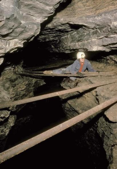 A caver moves across a metal pole above a canyon in the cave.