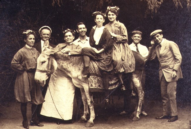 A black and white photo of a group of visitors posing with a donkey.
