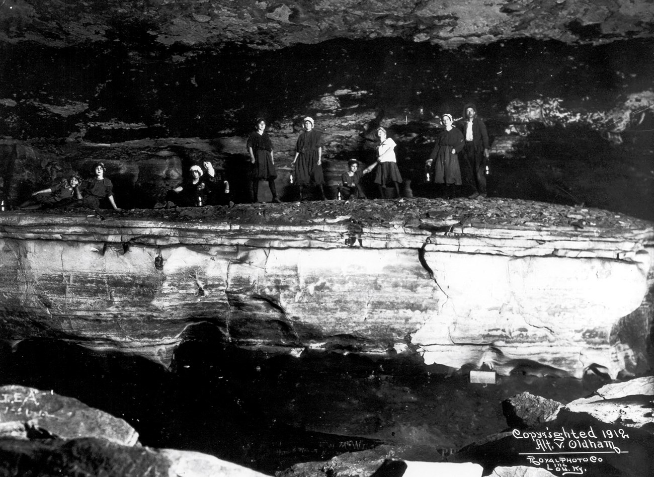 A black and white photo of people sitting on the top of a large rock in the cave.