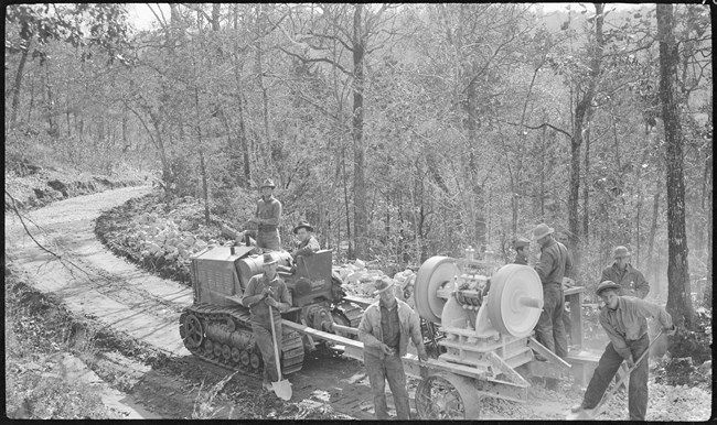 A black and whit photo of a bulldozer creating a road.