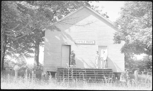 A black and white photo of three people standing in front of a small single room church.