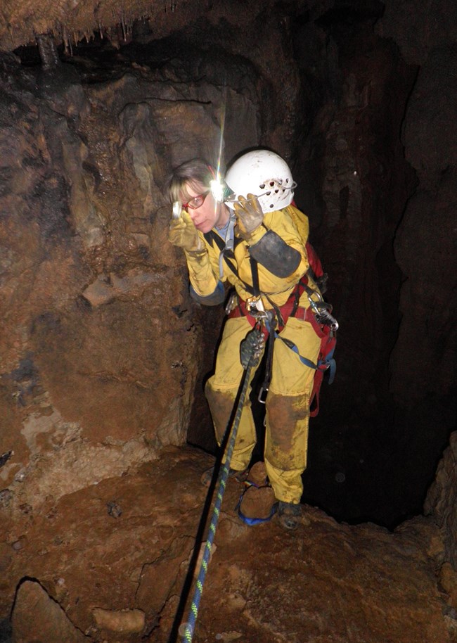 A cave researcher is secured on a rope while reading a instrument.