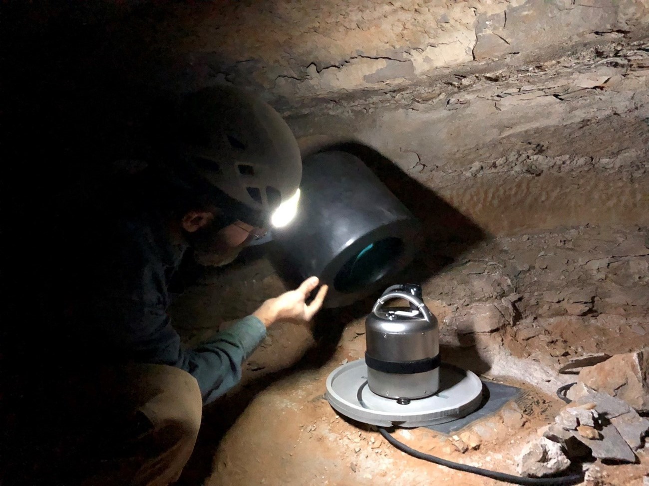 A man installs a shiny silver seismometer within a rocky cave.