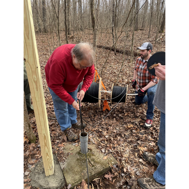 A man lowers power, communications, and GPS antenna cables down into the seismic station inside Mammoth Cave through a pipe known as the “Upside Down Well”.