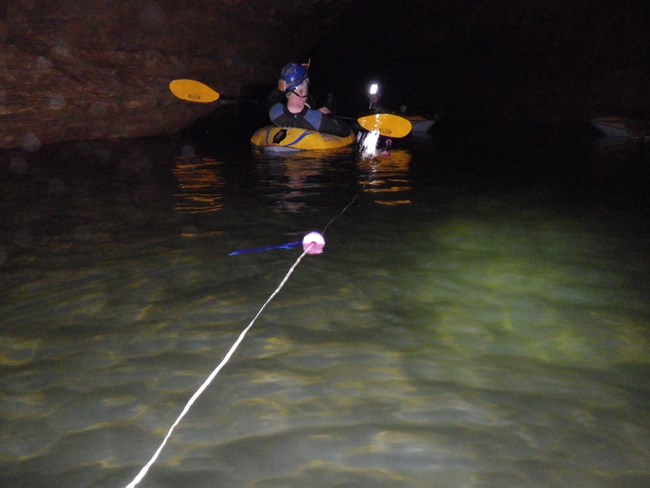 A cave researcher in a inflatable kayak on an undergrounds river