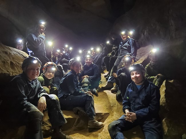 A group of school age kids in the cave with bright headlamps on.