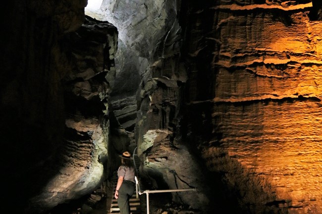 A person standing at the opening of a narrow cave passage.