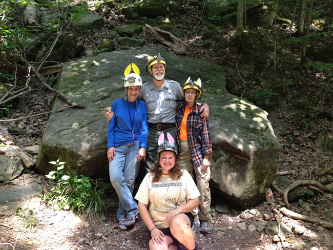 A park ranger and members of the NSS lint bunny crew pose in front of a large rock outside of the Historic Entrance