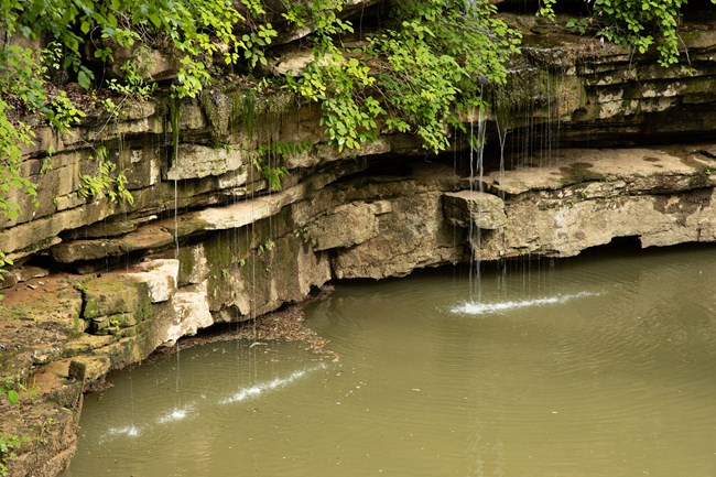 Water falling off of a rock ledge into a pool of water.