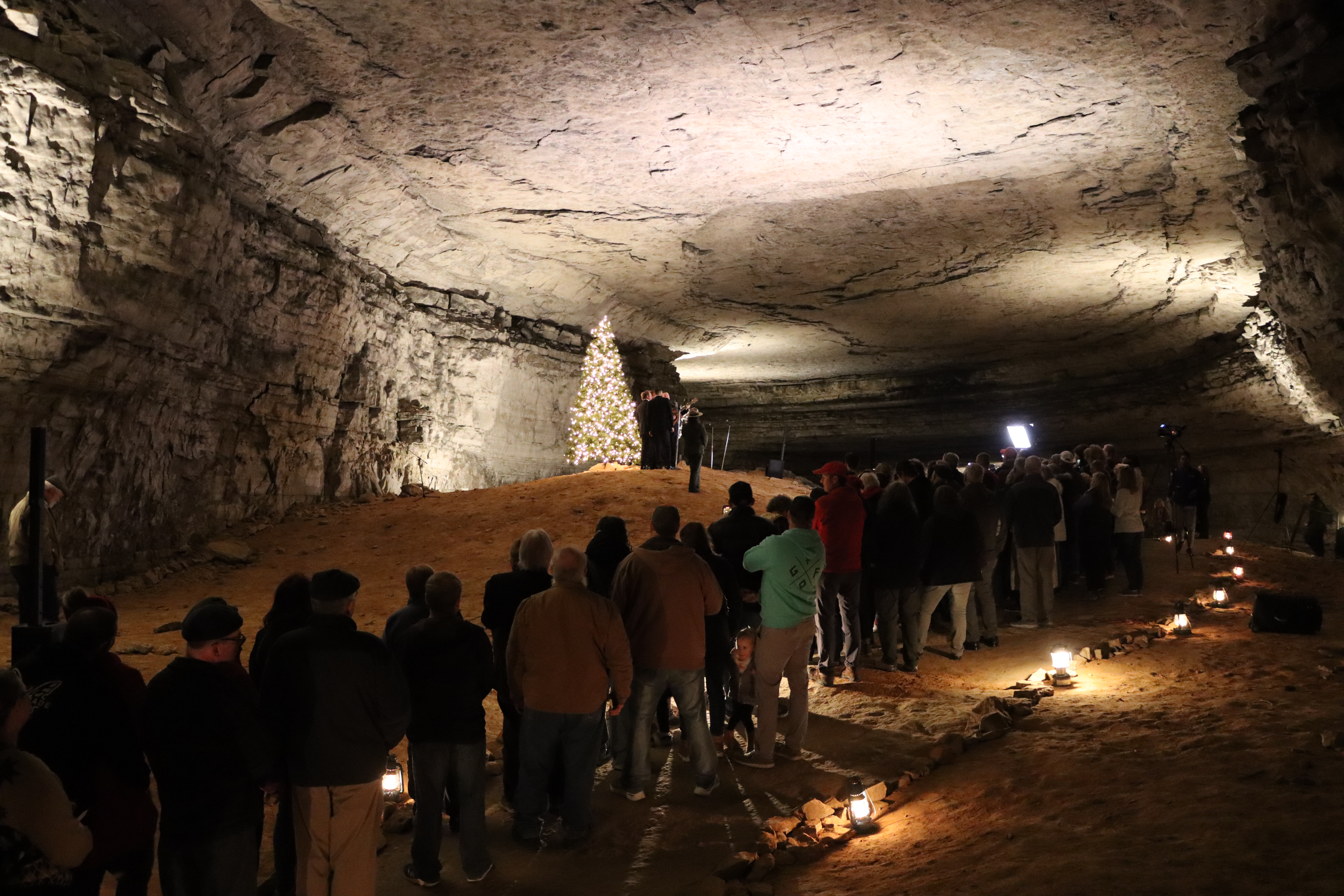 A group of people stand around an illuminated tree in a cave passageway.