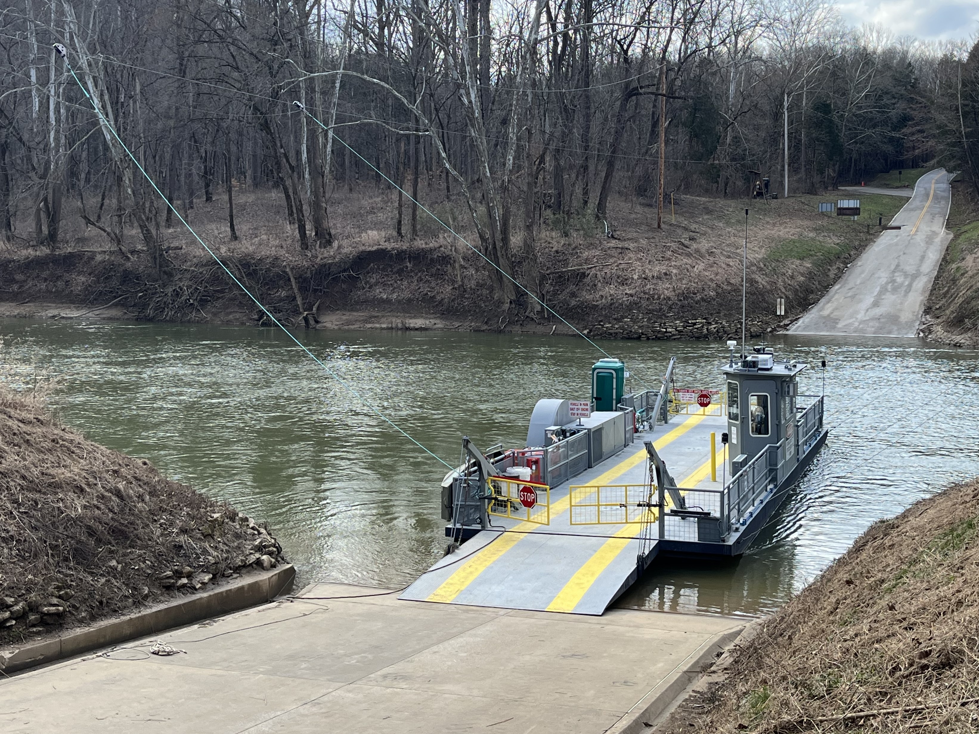 A cable ferry sits at the riverbank with its ramp down, guide cables overhead