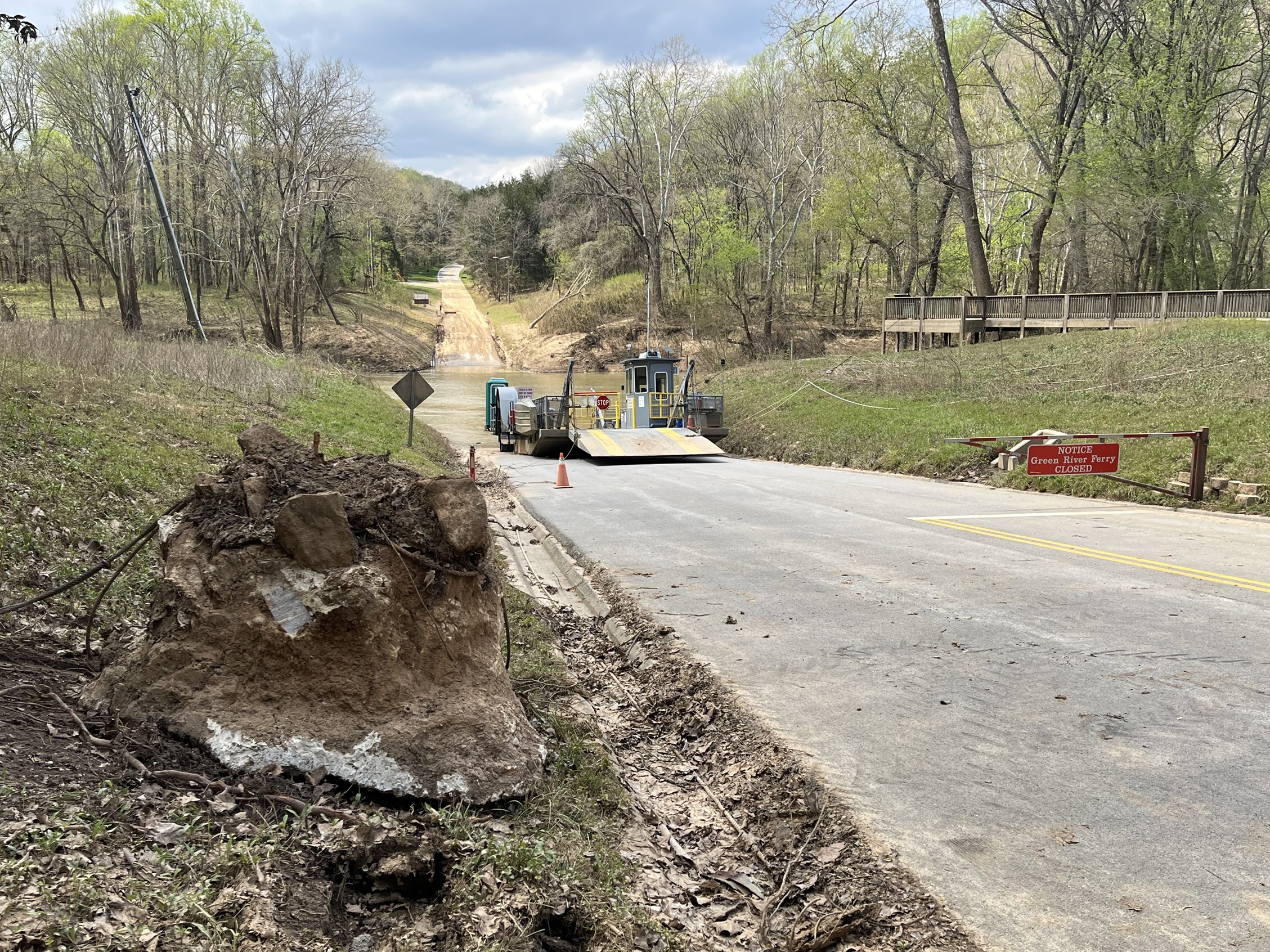 Historic flood damage at the Green River Ferry crossing. A large rock covered in dirt and loose cables sits on the ground in front of a large ferry boat.