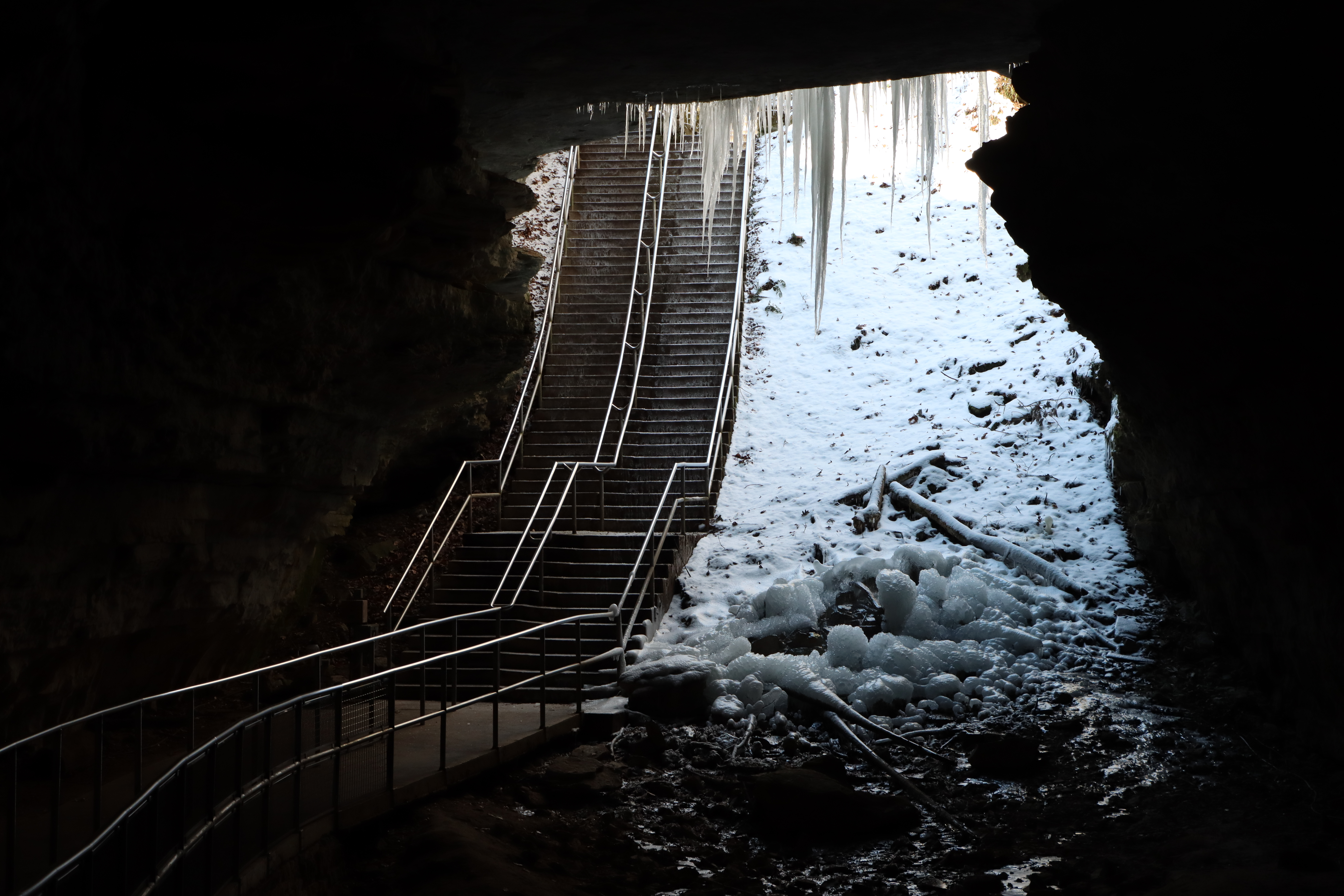 A long stairway descends down a snow-covered entrance to a cave.