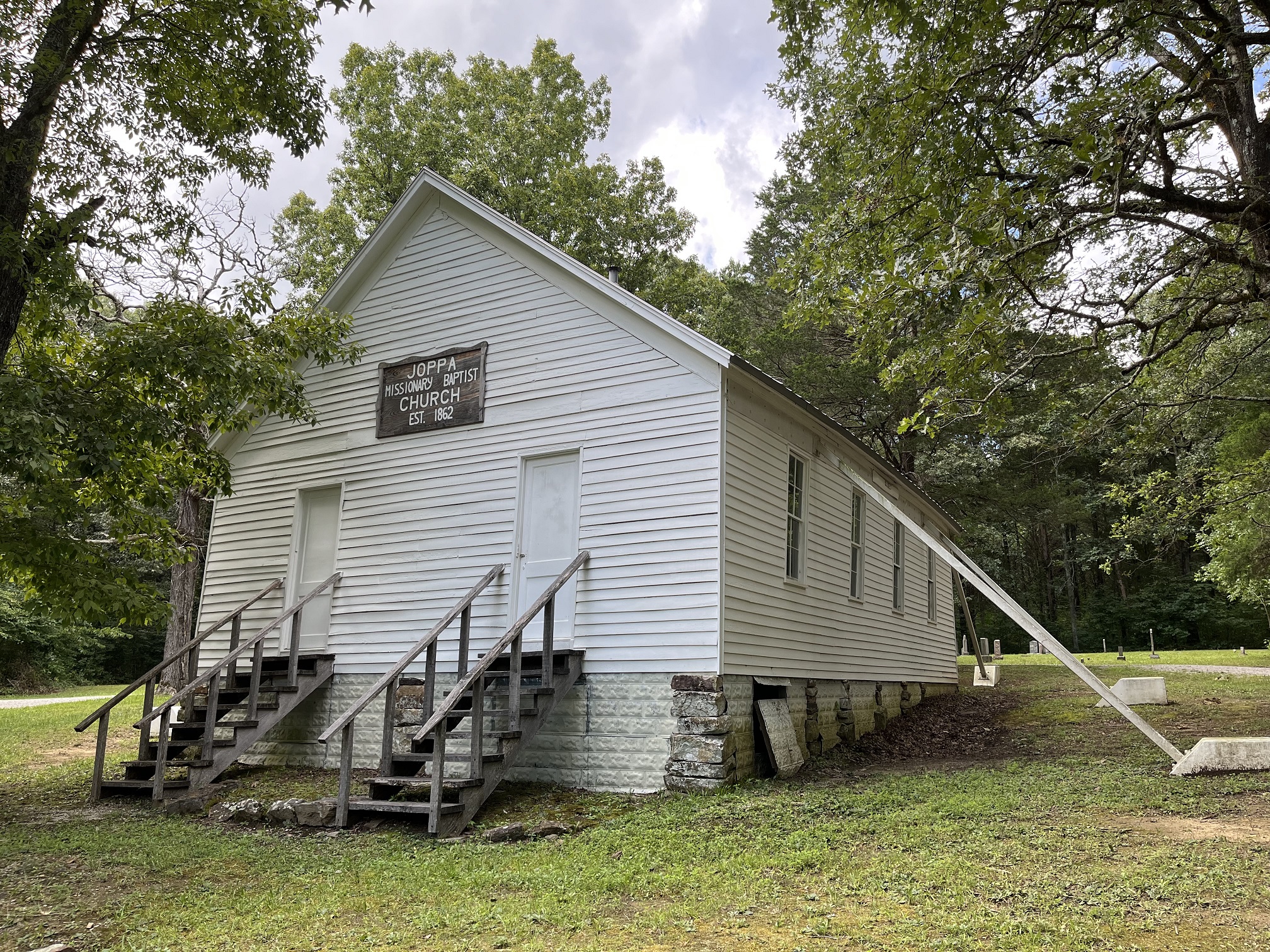 White sided building with long wooden staircases leading to two entry doors. A sign between the doors reads “Joppa Missionary Baptist Church Est. 1862.”